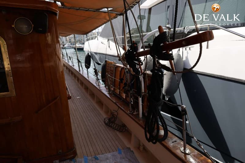 Een houten bootdek met een kajuit en een deel van een andere boot ernaast, met touwen en stootwillen.
