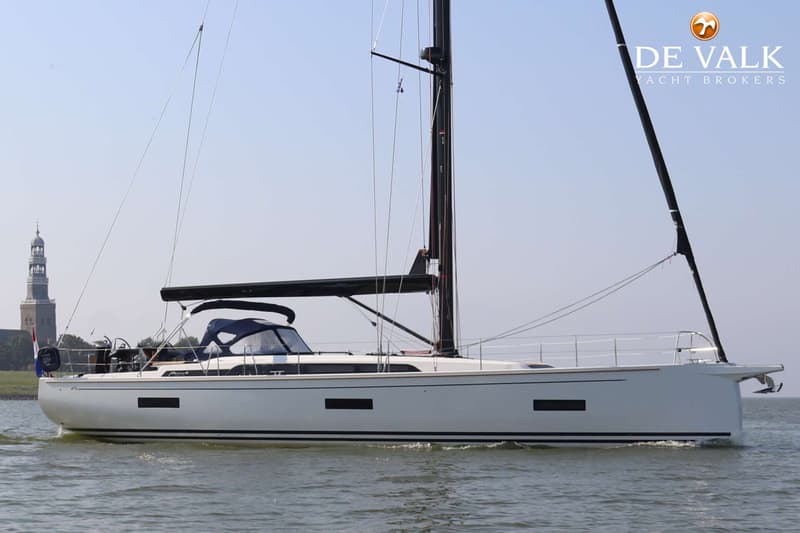 Een witte zeilboot met een zwarte mast en giek vaart op het water, met een toren in de verte. — Arcona 50