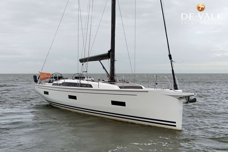 Een witte zeilboot met zwarte strepen op de romp en een oranje vlag met "DE VALK YACHT BROKERS" vaart op water. — Arcona 50