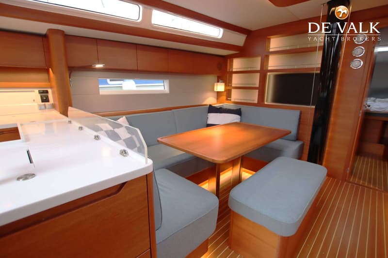 Een kajuit met houten vloer en wanden, een U-vormige bank met grijze kussens, een houten tafel en een aanrecht. — Arcona 50