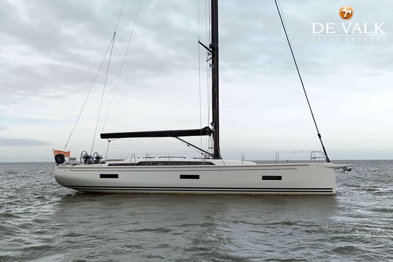 Een witte zeilboot met zwarte strepen op de romp en een zwarte mast en giek, drijvend op water onder een bewolkte lucht.