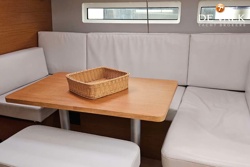 Een interieur met een houten tafel, omringd door witte banken en kussens, met ramen erboven.