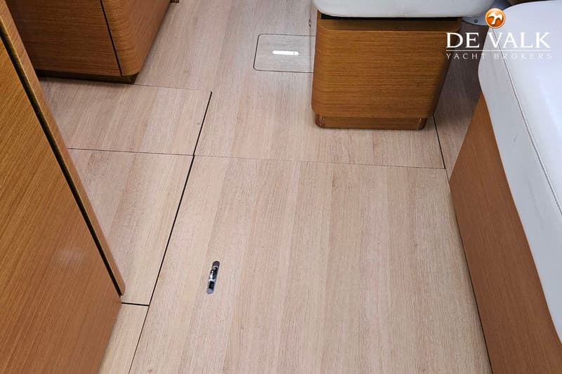 De foto toont een houten vloer met een metalen handvat en houten meubels met witte bekleding.