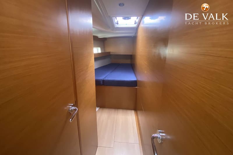 Een kajuit met een tweepersoonsbed met blauwe matrassen, houten wanden en vloer, en een dakluik. — Jeanneau Sun Odyssey 490