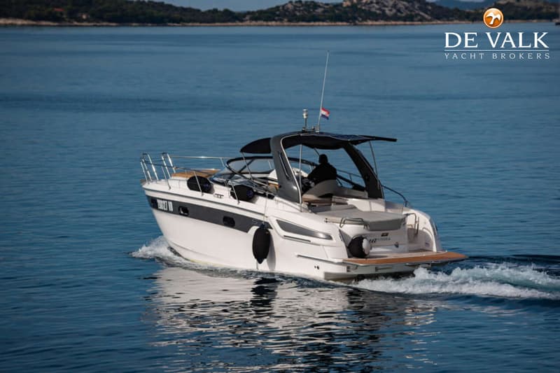 Een witte motorboot met een zwarte streep vaart over blauw water, met een persoon aan het roer en een vlag op het dak.