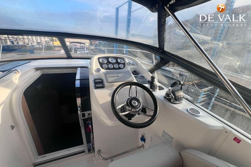 De foto toont de stuurstand van een boot met een stuurwiel, diverse meters, een Garmin-apparaat en een schuifdeur naar de…