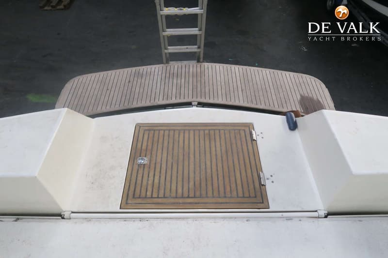 Een bovenaanzicht van het achterdek van een boot met een houten luik en een ladder die naar beneden leidt.