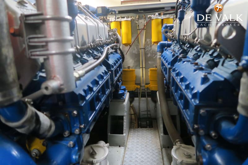 Twee grote blauwe scheepsmotoren met zilverkleurige en gele onderdelen zijn zichtbaar in een machinekamer.