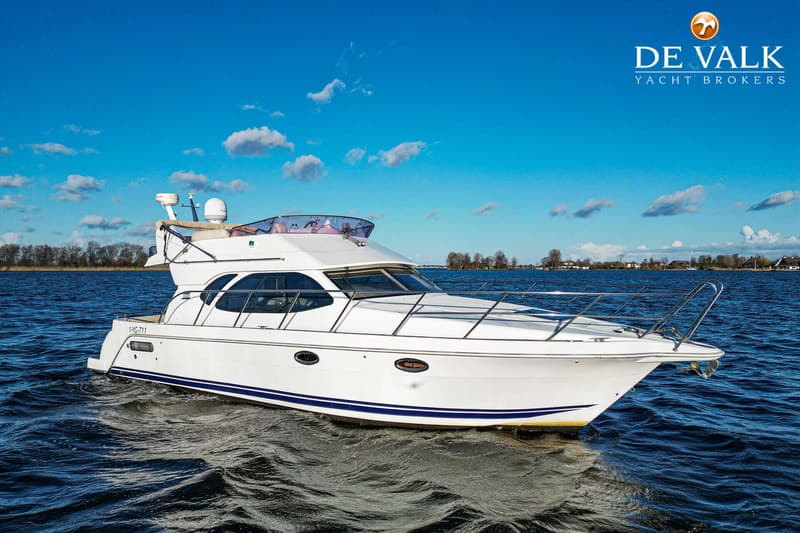 Een witte motorboot met blauwe strepen vaart op een waterweg onder een helderblauwe lucht met witte wolken. — Galeon 380 Fly