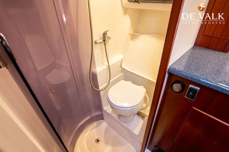 Een compacte badkamer met een toilet en een douchekop aan de muur, met een afvoer in de vloer.