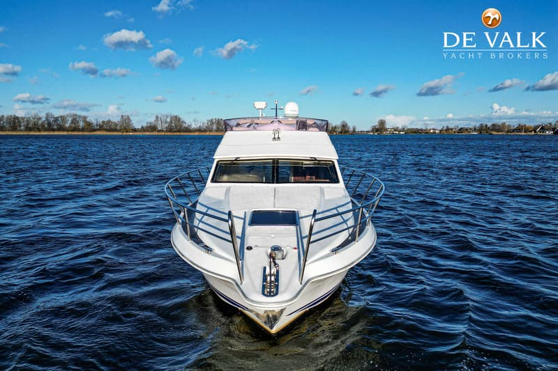 Een witte motorboot met blauwe strepen vaart op een meer onder een blauwe lucht met witte wolken. — Galeon 380 Fly
