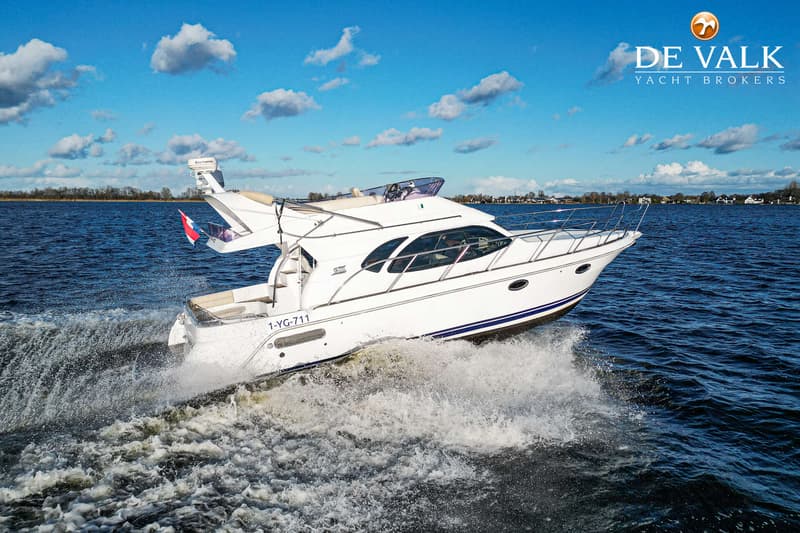 Een witte motorboot met blauwe strepen vaart over het water en creëert een kielzog, onder een blauwe lucht met wolken.