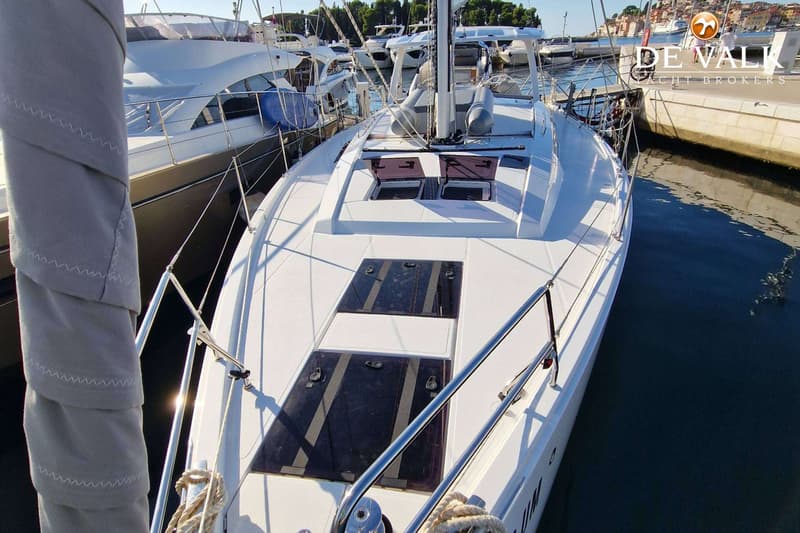 Een witte zeilboot ligt aangemeerd in een haven, met andere boten en gebouwen op de achtergrond. — Hanse 460
