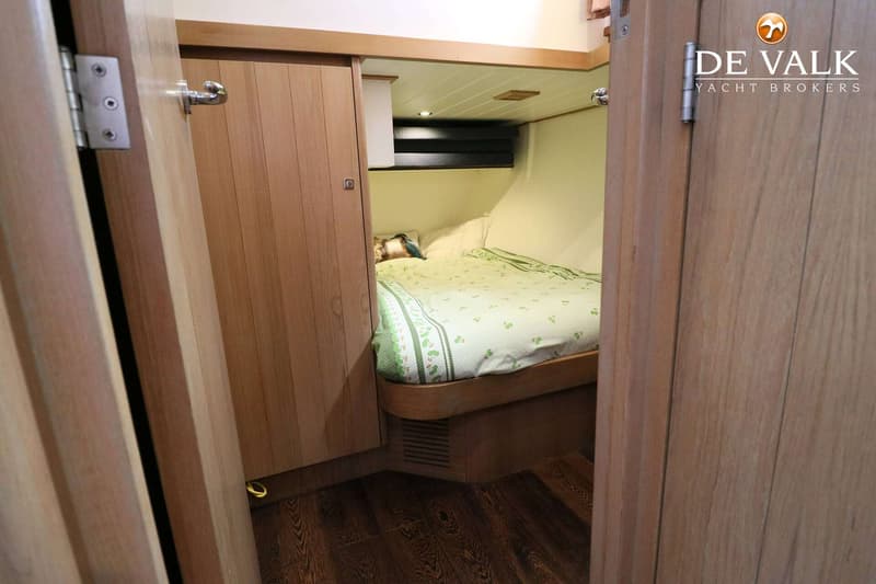 Een slaapkamer in een boot met een bed met groen dekbed, houten wanden en een donkere houten vloer. — Noordkaper 48 -S