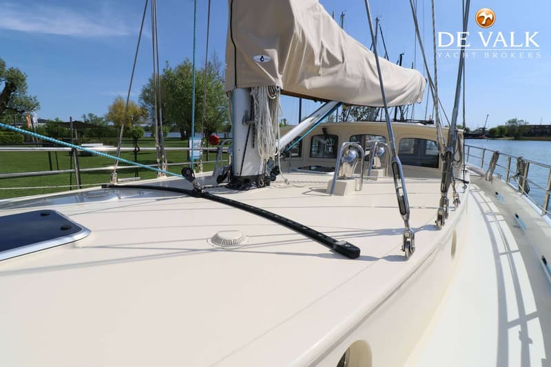 Een bovenaanzicht van het dek van een zeilboot met een opgerold zeil en mast, met een waterweg en groen gras op de…