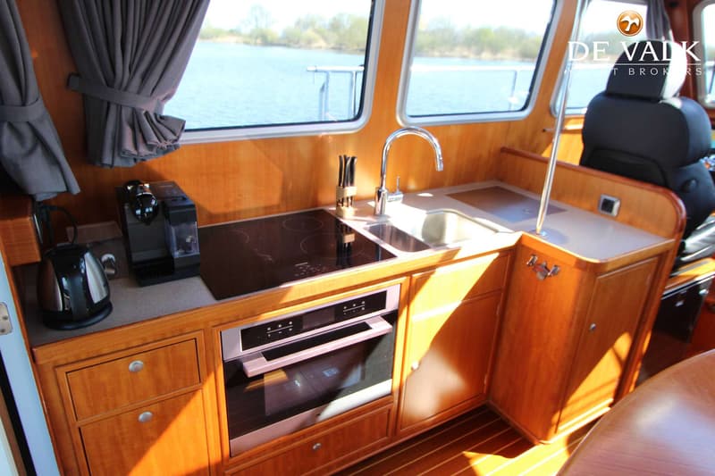 Een kombuis met houten kasten, een kookplaat, spoelbak, oven, koffiezetapparaat en waterkoker.