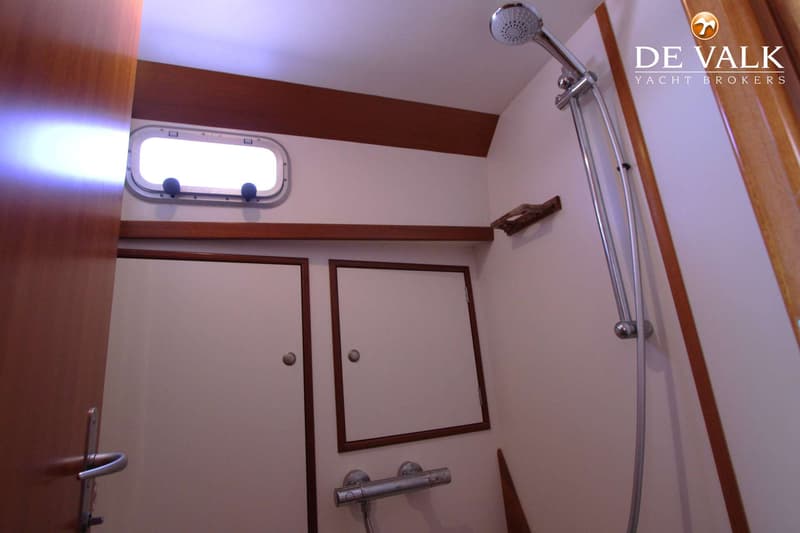 Een interieur van een boot met een patrijspoort, twee kastdeurtjes, een douchekop en een thermostaatkraan.