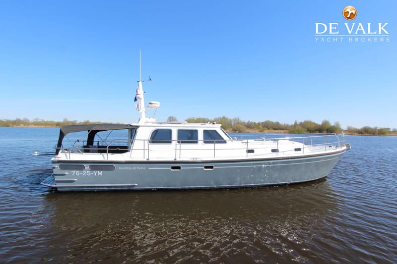 Een grijze en witte motorboot met registratienummer 76-25-YM vaart op een meer onder een heldere blauwe lucht.