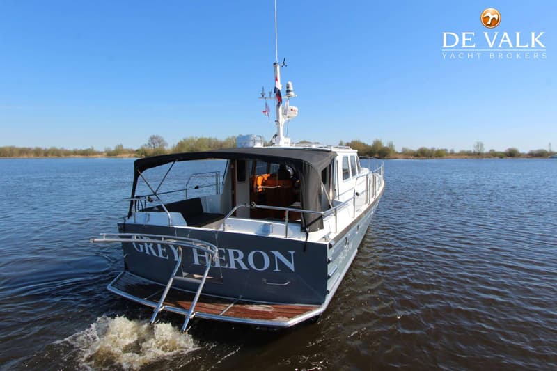 Een motorjacht met de naam "GREY HERON" vaart op een waterweg, gezien vanaf de achtersteven.