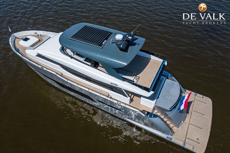Een grote, grijze en witte motorjacht met een Nederlands vlaggetje aan de achtersteven, gezien van bovenaf op het water.