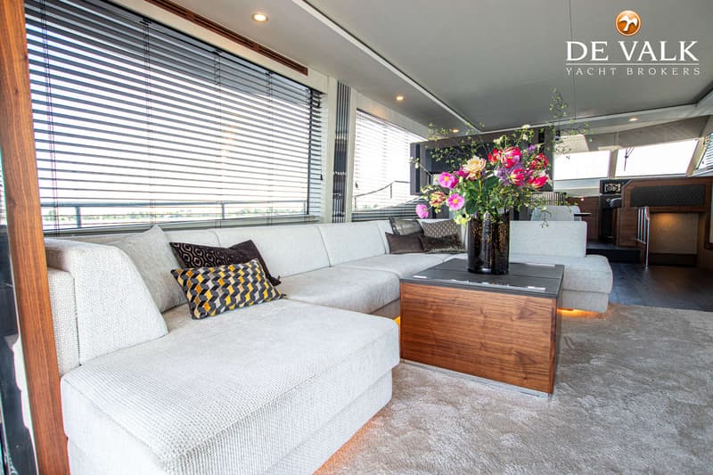 Een interieur van een boot met een grote L-vormige bank, een salontafel met bloemen en een tapijt.