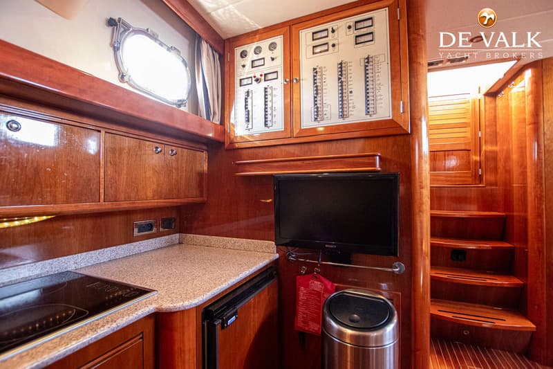 De foto toont een interieur van een boot met houten afwerking, een kombuis met kookplaat en een trap naar een ander dek.