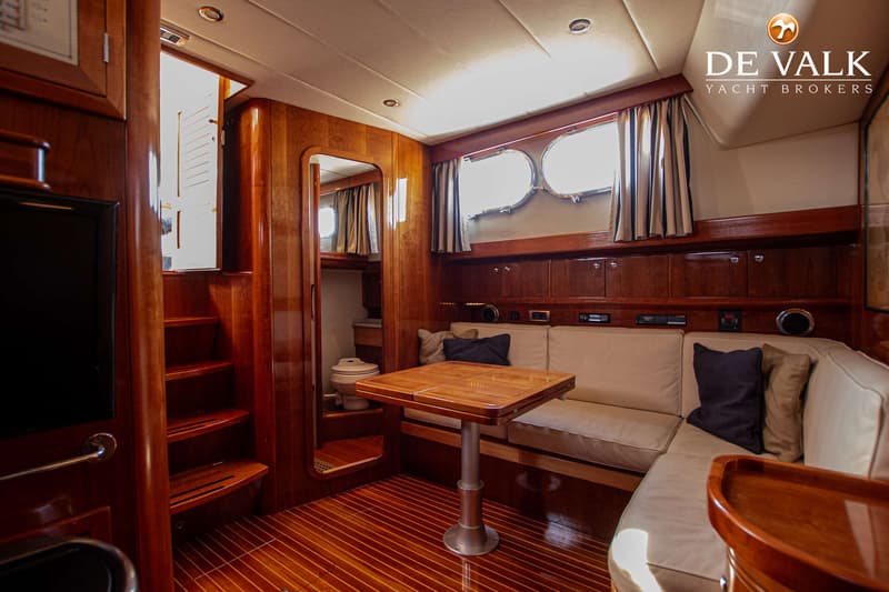 De foto toont een houten interieur van een boot met een zithoek, tafel, trap en een toiletruimte. — Apreamare 12