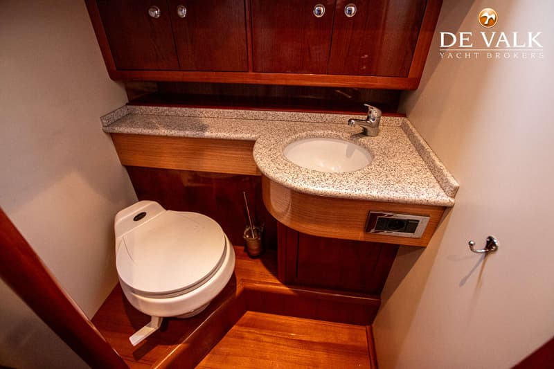 De foto toont een badkamer met een wit toilet, een wastafel met kraan en een aanrechtblad met spikkels.
