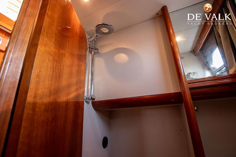 Een douchekop met slang hangt aan de wand in een kajuit met houten en witte panelen, en een spiegel. — Apreamare 12