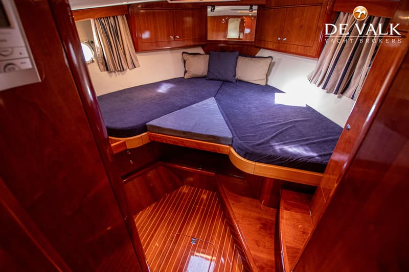 De foto toont een kajuit met een V-vormig bed, donkerblauwe kussens, houten lambrisering en een spiegel. — Apreamare 12