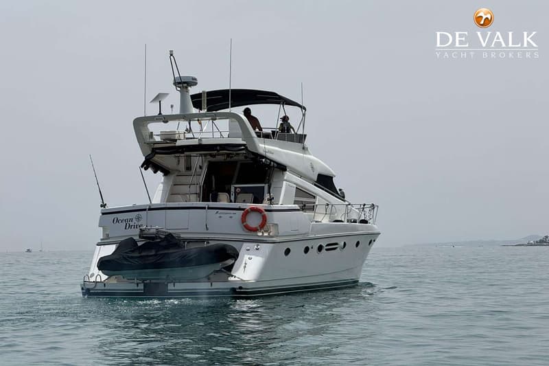Een witte motorboot met de naam "Ocean Drive" op de spiegel, een bijboot en twee personen op het bovendek. — Johnson 56