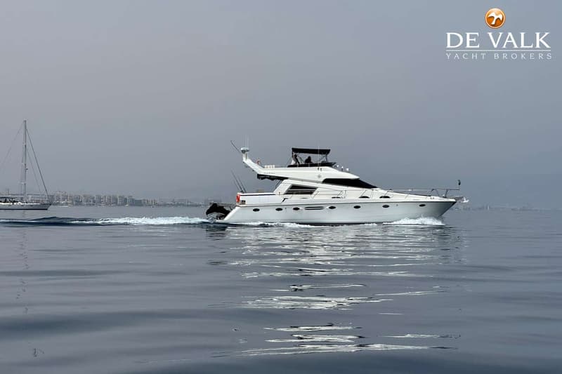 Een witte motorboot vaart op rustig water, met een zeilboot en een stad aan de horizon. — Johnson 56