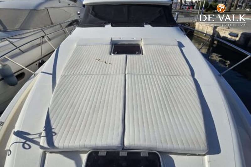 De foto toont het voordek van een boot met vier witte kussens, een luik en een zwart afdekzeil. — Johnson 56