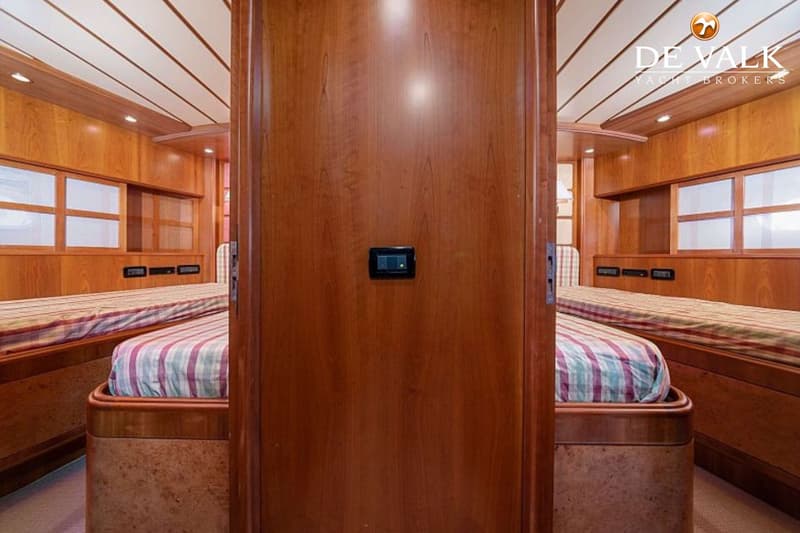Een houten kajuit met twee bedden met gestreepte dekens, gescheiden door een houten wand met een schakelaar.