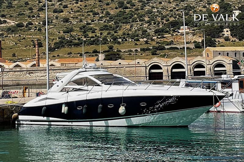 Een witte en donkerblauwe motorboot ligt aangemeerd in een haven met een bergachtige achtergrond. — Sunseeker Portofino 53