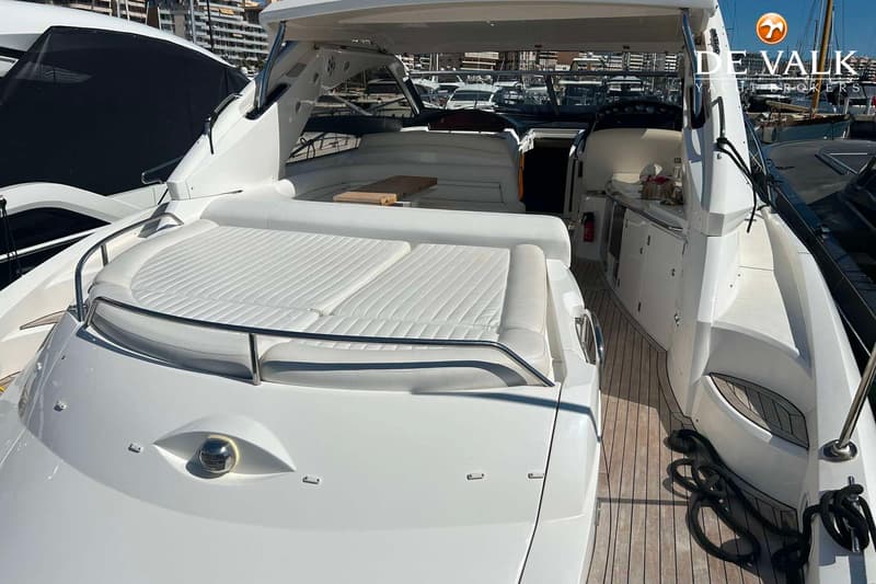 Een witte motorboot met een teakhouten dek en witte kussens ligt in een haven. — Sunseeker Portofino 53