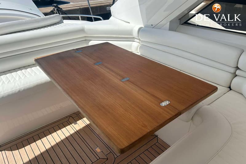 Een houten tafel met metalen scharnieren, omringd door witte kussens en een houten vloer.
