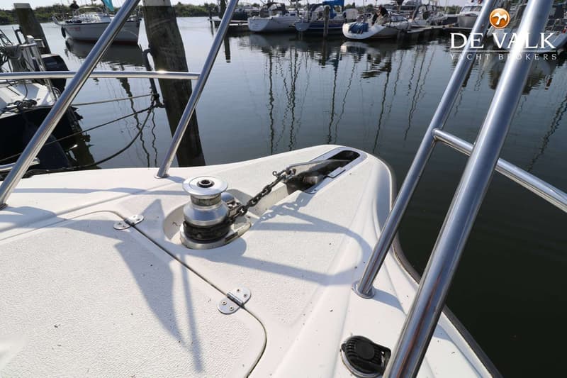 De foto toont de boeg van een witte boot met een ankerlier en ankerketting, met op de achtergrond andere boten in een haven.