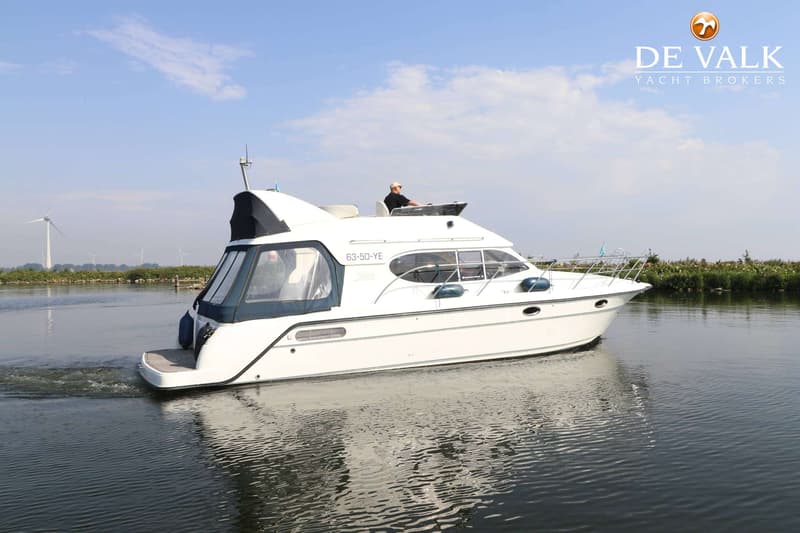 Een witte motorboot met een man aan het roer vaart op rustig water, met windmolens op de achtergrond. — Galeon 380 Fly