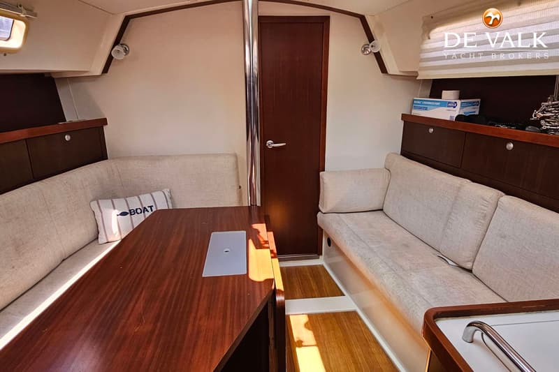 De foto toont een kajuit met een houten tafel, twee banken met lichte kussens, een deur en een kast. — Hanse 350