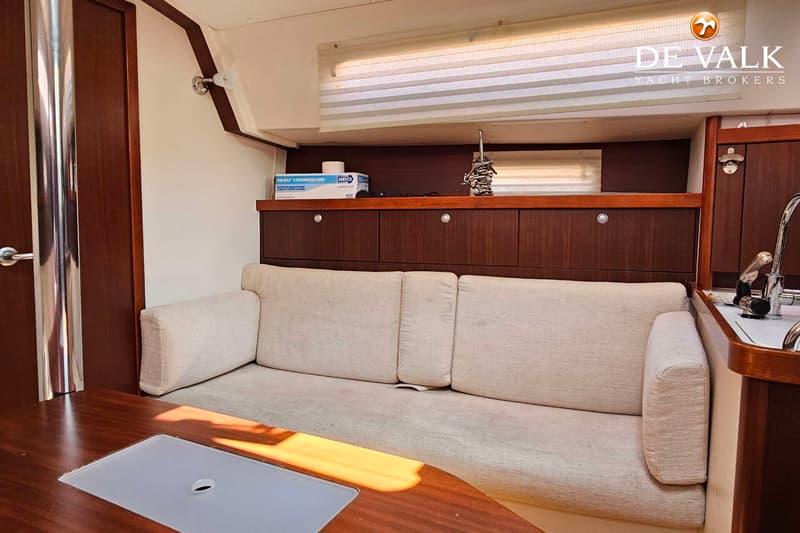Een interieur van een boot met een beige bank, houten kasten en een tafel met een ingebouwde gootsteen. — Hanse 350