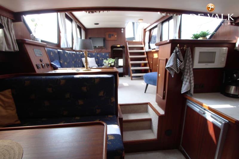 De foto toont het interieur van een boot met een zithoek, kombuis en trap naar een hoger dek. — Valkkruiser 1350