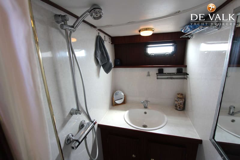 Een badkamer met een douche, wastafel, spiegel, handdoek en een pot met schelpen.