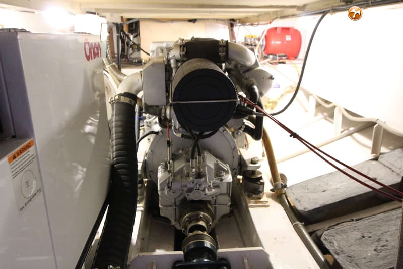 Een motorruimte met een grote grijze motor, een wit Onan-aggregaat en een rode tank.