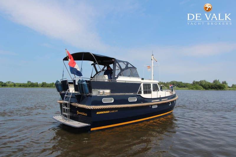Een donkerblauwe motorboot met witte opbouw en gele streep vaart op het water onder een blauwe lucht.