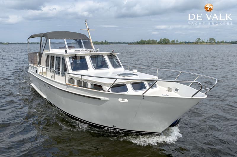 Een witte motorboot met een zwarte kap vaart op een waterweg onder een bewolkte hemel. — Almkruiser 12.65