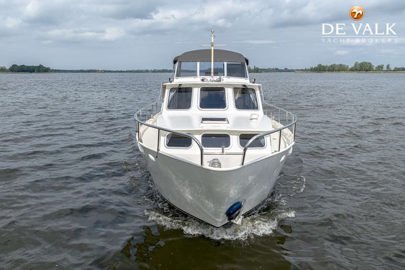 Een witte motorboot vaart op een waterweg met een bewolkte lucht en bomen op de achtergrond. — Almkruiser 12.65