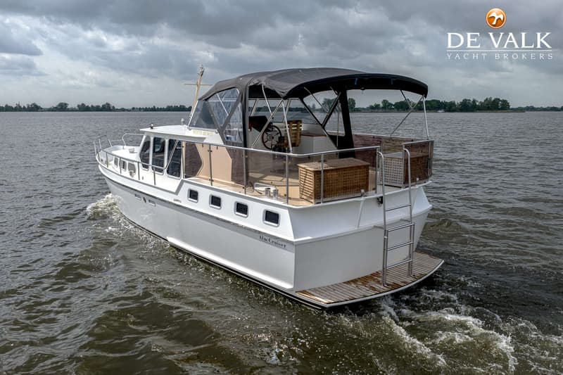 Een witte motorboot met een zwarte kap vaart op water onder een bewolkte lucht, met land in de verte. — Almkruiser 12.65