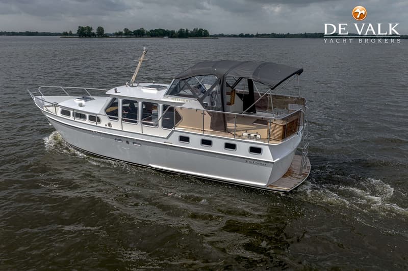 Een witte motorboot met een donkergrijze bimini vaart op een waterweg onder een bewolkte hemel. — Almkruiser 12.65