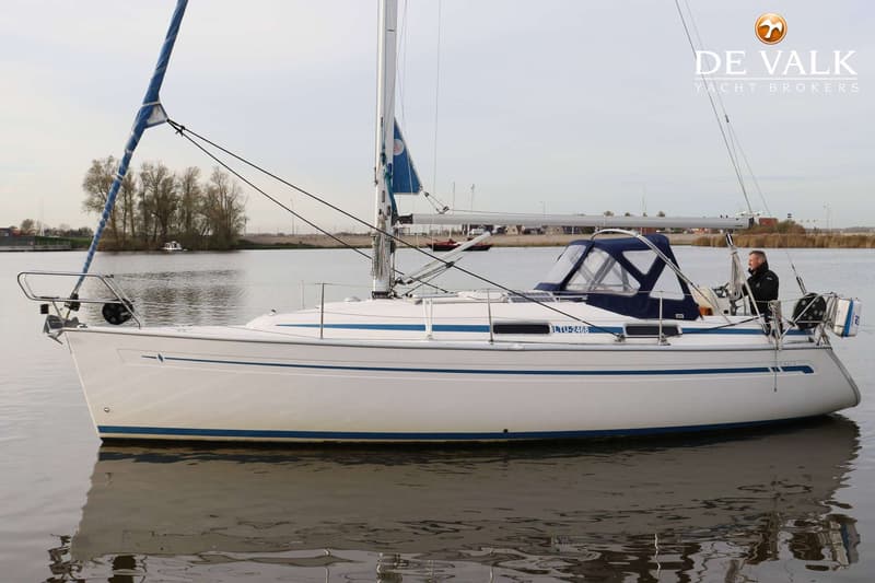 Een witte zeilboot met blauwe strepen en een blauwe buiskap ligt in het water. — Bavaria 31